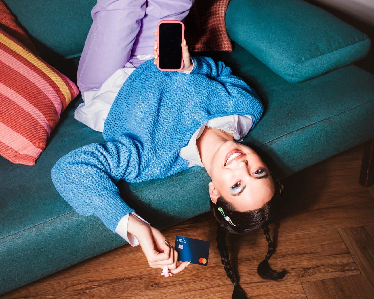Una mujer recostada en un sillón mira su celular con una tarjeta Nelo en la mano